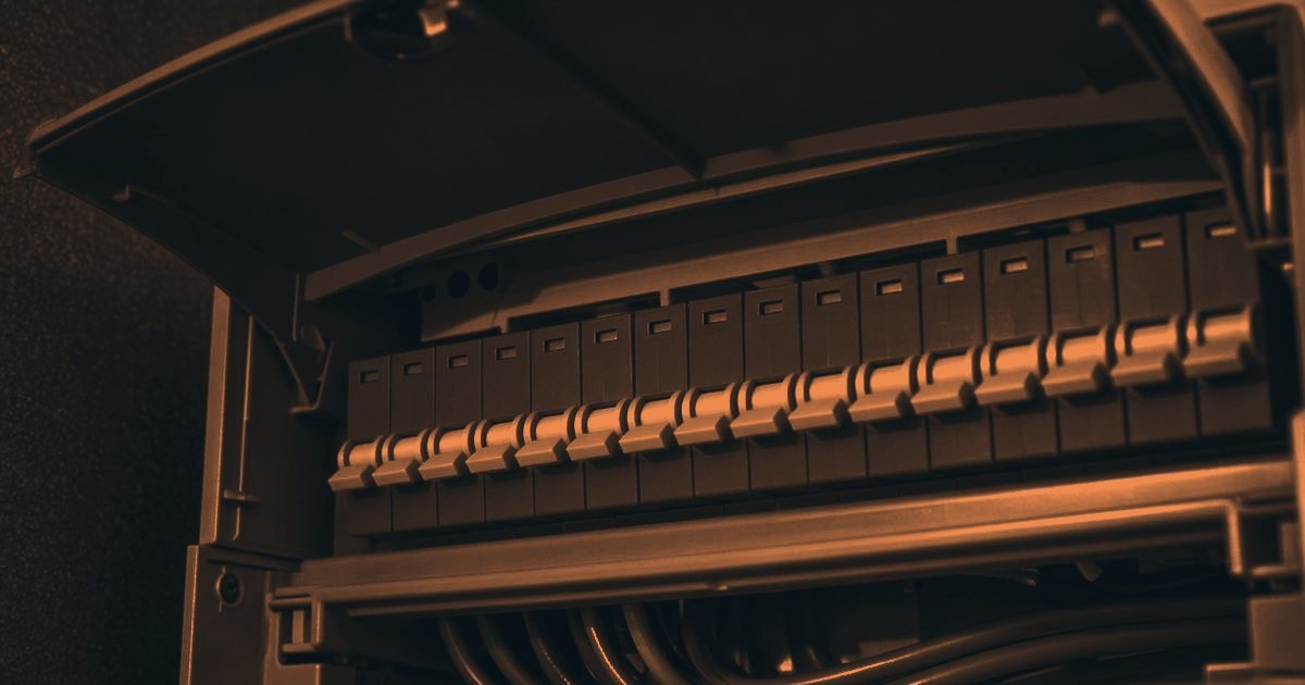 A domestic consumer unit with its cover open and a neat row of circuit breakers in a charcoal and orange duotone