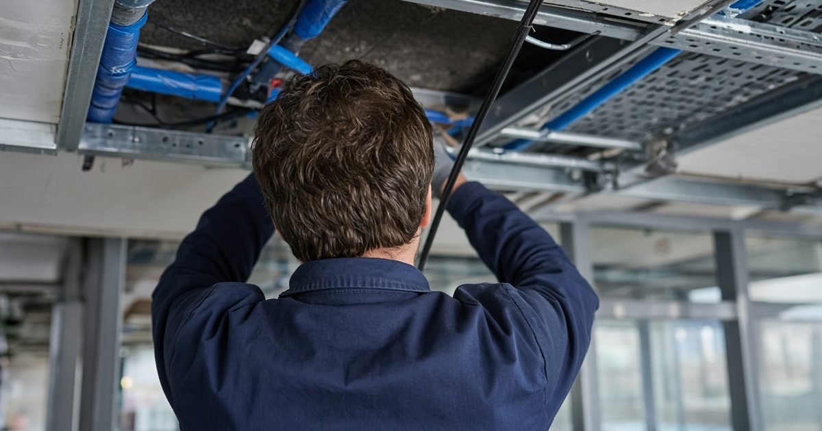 An electrician, seen from behind, working beside electrical cable and tools on site in daylight